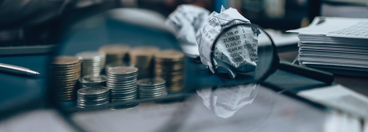Vergrootglas vergroot een stapel munten en een prop paier met allerlei kosten erop